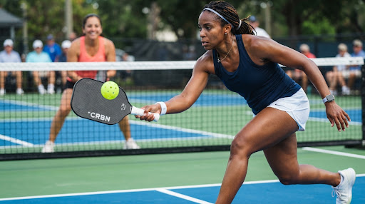 A player lunging forward to reach a low ball just behind the kitchen line on a blue outdoor pickleball court